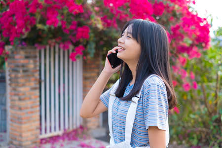 Young Asian girl talking on the phone outdoor, beautiful flower background.の写真素材