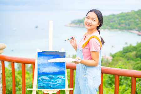 Young girl using brush drawing picture on canvas paper, at beautiful landscape view at koh tao Thailand.の写真素材