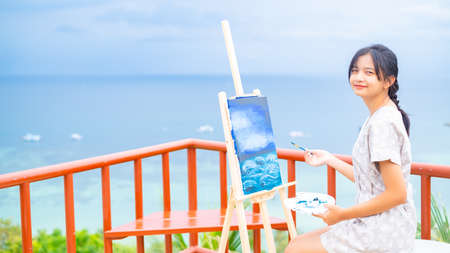 Young girl using brush drawing picture on canvas paper, at beautiful landscape view at koh tao Thailand.の写真素材