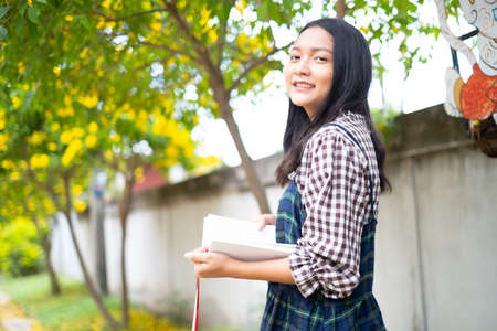 A young girl holds a book and standing under a beautiful tree.の写真素材