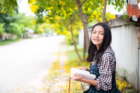 Young girl sitting on a bench reading a book under a beautiful tree.の写真素材