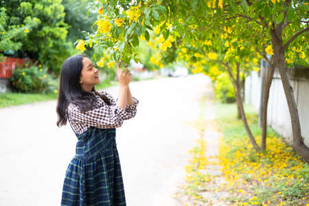 Young girl standing under yellow floawer tree.