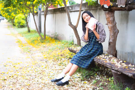 Young girl sitting on a bench reading a book under a beautiful tree.の写真素材