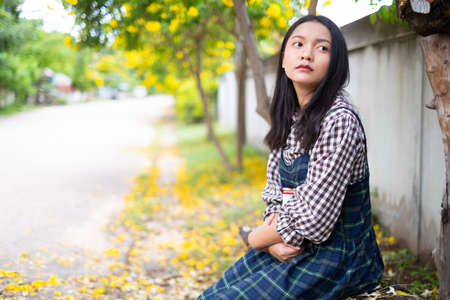 Young girl sitting on a bench reading a book under a beautiful tree.の写真素材