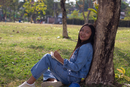 Cheerful young sitting in the park sketching picture,wears jacket and jeans. City life conceptの写真素材