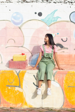 The cheerful girl wearing party hat with gift box sitting on colorful background.の写真素材