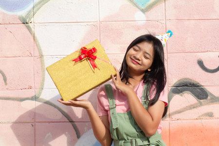 The cheerful girl wearing party hat with gift box sitting on colorful background.の写真素材