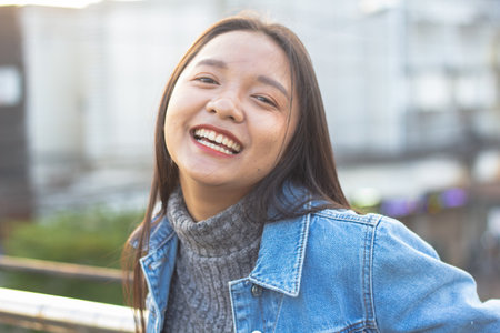 Close-up portrait of laughing long hair  girl in jacket jeans on city background. Smart girl standing on bridge, Lifestyle concept.の写真素材
