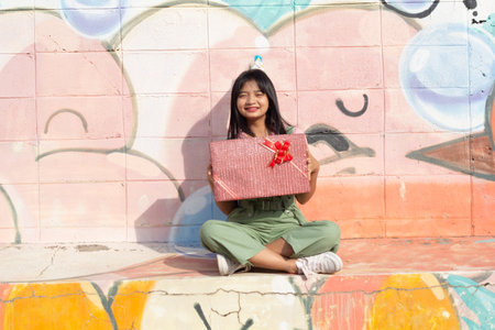The cheerful girl wearing party hat with gift box sitting on colorful background.の写真素材