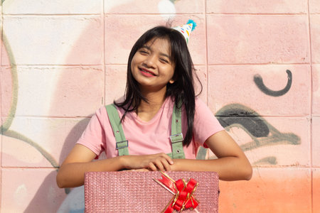 The cheerful girl wearing party hat with gift box sitting on colorful background.の写真素材