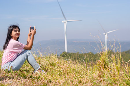 Young girl standing on the mountain taking beautiful landscape view and the Wind Turbine at Khao Yai Thieng Electric Wind Turbine Thailand.の写真素材