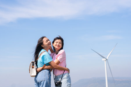 Happy two girls standing together looking at the wind turbines and mountain with blue sky. Khao Yai Thieng Electric Wind Turbine Thailand.の写真素材