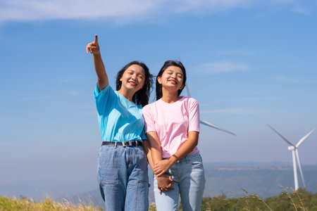 Happy two girls standing together looking at the wind turbines and mountain with blue sky. Khao Yai Thieng Electric Wind Turbine Thailand.の写真素材