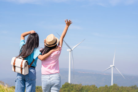 Happy two girls standing together looking at the wind turbines and mountain with blue sky. Khao Yai Thieng Electric Wind Turbine Thailand.の写真素材