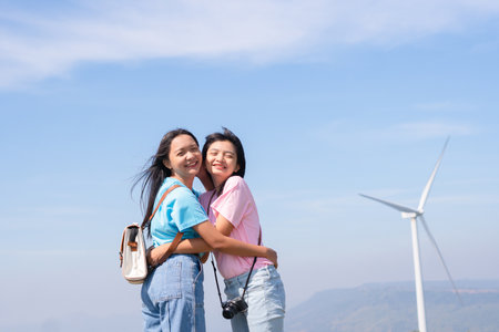 Happy two girls standing together looking at the wind turbines and mountain with blue sky. Khao Yai Thieng Electric Wind Turbine Thailand.の写真素材