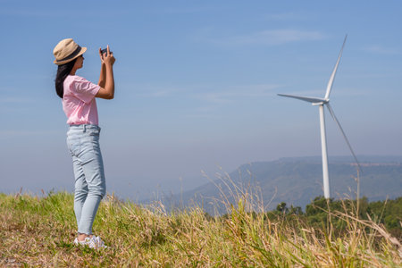 Young girl standing on the mountain taking beautiful landscape view and the Wind Turbine at Khao Yai Thieng Electric Wind Turbine Thailand.の写真素材