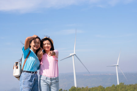 Happy two girls standing together looking at the wind turbines and mountain with blue sky. Khao Yai Thieng Electric Wind Turbine Thailand.の写真素材