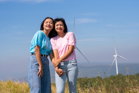 Happy two girls standing together looking at the wind turbines and mountain with blue sky. Khao Yai Thieng Electric Wind Turbine Thailand.の写真素材