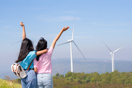 Happy two girls standing together looking at the wind turbines and mountain with blue sky. Khao Yai Thieng Electric Wind Turbine Thailand.の写真素材