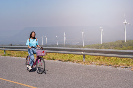 Young girl ride a bike on the road at the mountain with Wind Turbine, Khao Yai Thieng Electric Wind Turbine Thailand.の写真素材