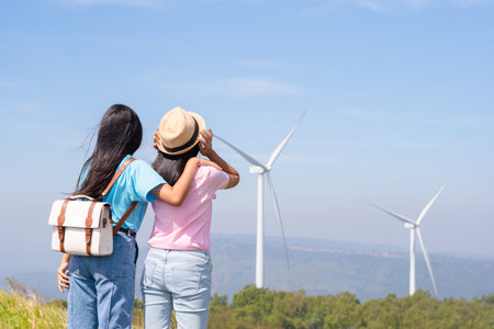 Happy two girls standing together looking at the wind turbines and mountain with blue sky. Khao Yai Thieng Electric Wind Turbine Thailand.の写真素材