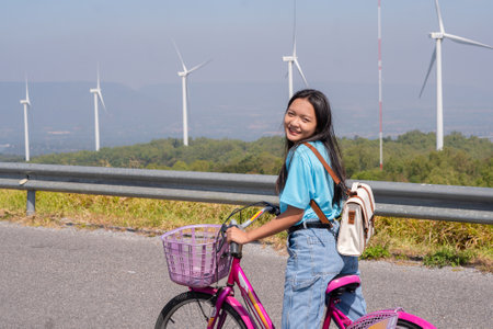 Young girl ride a bike on the road at the mountain with Wind Turbine, Khao Yai Thieng Electric Wind Turbine Thailand.の写真素材