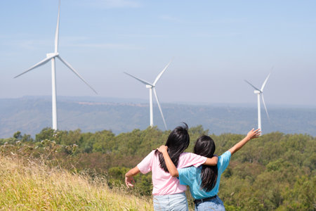 Happy two girls standing together looking at the wind turbines and mountain with blue sky. Khao Yai Thieng Electric Wind Turbine Thailand.の写真素材