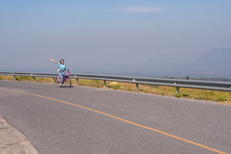 Young girl ride a bike on the road at the mountain with Wind Turbine, Khao Yai Thieng Electric Wind Turbine Thailand.の写真素材