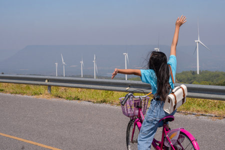 Young girl ride a bike on the road at the mountain with Wind Turbine, Khao Yai Thieng Electric Wind Turbine Thailand.の写真素材
