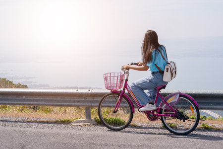 Young girl ride a bike on the road at the mountain with Wind Turbine, Khao Yai Thieng Electric Wind Turbine Thailand.の写真素材