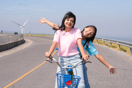 Two Young girl ride a bike on the road at the mountain with Wind Turbine, Khao Yai Thieng Electric Wind Turbine Thailand.の写真素材