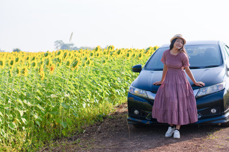 Beautiful young girl standing beside the car in the sunflowers field. Summer time.の写真素材