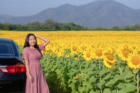 Beautiful young girl standing beside the car in the sunflowers field. Summer time.の写真素材