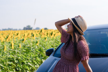 Beautiful young girl standing beside the car in the sunflowers field. Summer time.の写真素材