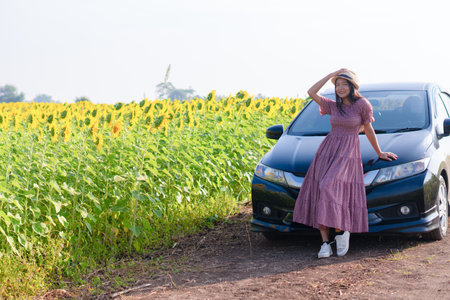Beautiful young girl standing beside the car in the sunflowers field. Summer time.の写真素材