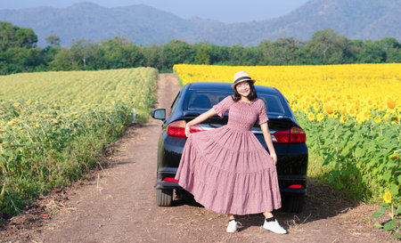 Beautiful young girl standing beside the car in the sunflowers field. Summer time.の写真素材