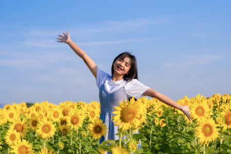 Cute young girl standing in the sunflowers field with blue sky on vacation time.の写真素材