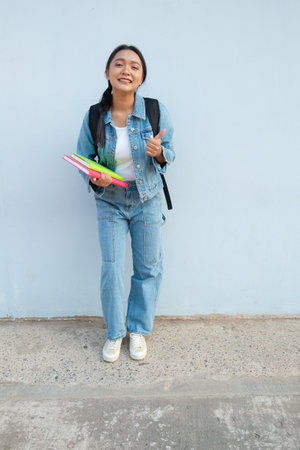 Student young girl standing at school wear jean hold book with backpack, blue background.の写真素材