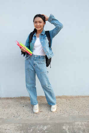 Student young girl standing at school wear jean hold book with backpack, blue background.の写真素材