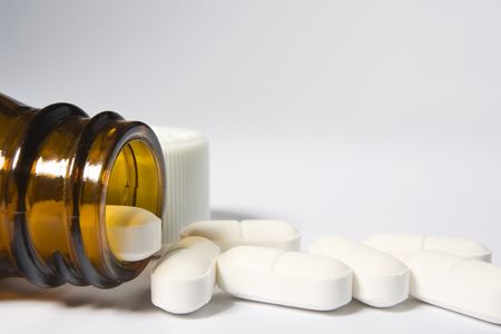 The mouth of a bottle on the left-hand side of a white background with a row of pills arranged along the bottom of the frameの写真素材
