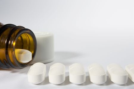 The mouth of a bottle on the left-hand side of a white background with a row of pills arranged along the bottom of the frameの写真素材