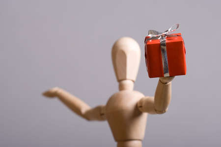Wooden marionette presenting a red gift. Short DOF.の写真素材