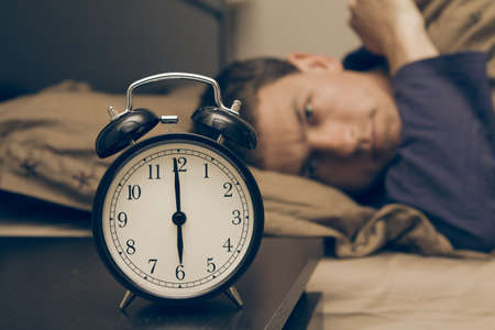 Alarm clock with male model in bed in background. Shallow depth of field.の写真素材