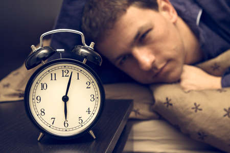 Alarm clock with male model in bed in background. Shallow depth of field.の写真素材