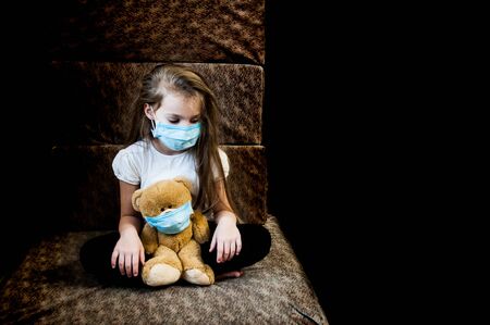 Sad child girl in a protective mask with her favorite toy. During illness. Epidemics coronavirus, flu and children. Stress and despair for children. Left alone.の写真素材