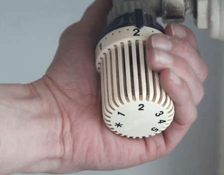 Hand puts the temperature in a white heating thermostat の写真素材