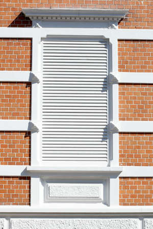 Old ornate window with white shutters on a red brick wall