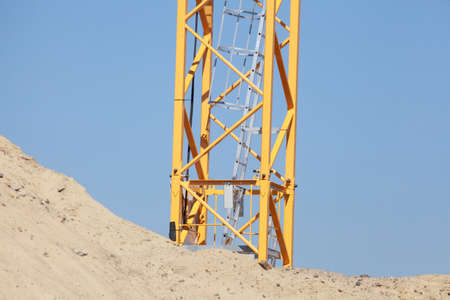 Yellow construction crane and sand hill on a construction site, blue skyの写真素材