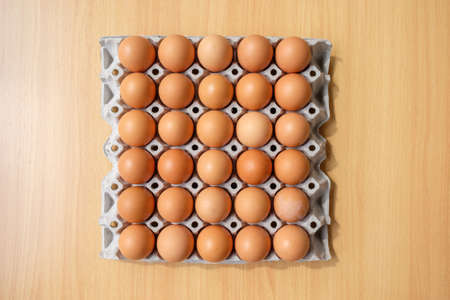 A dozen brown eggs in a carton on a wooden tableの写真素材