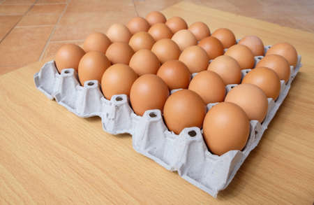 A dozen brown eggs in a carton on a wooden table